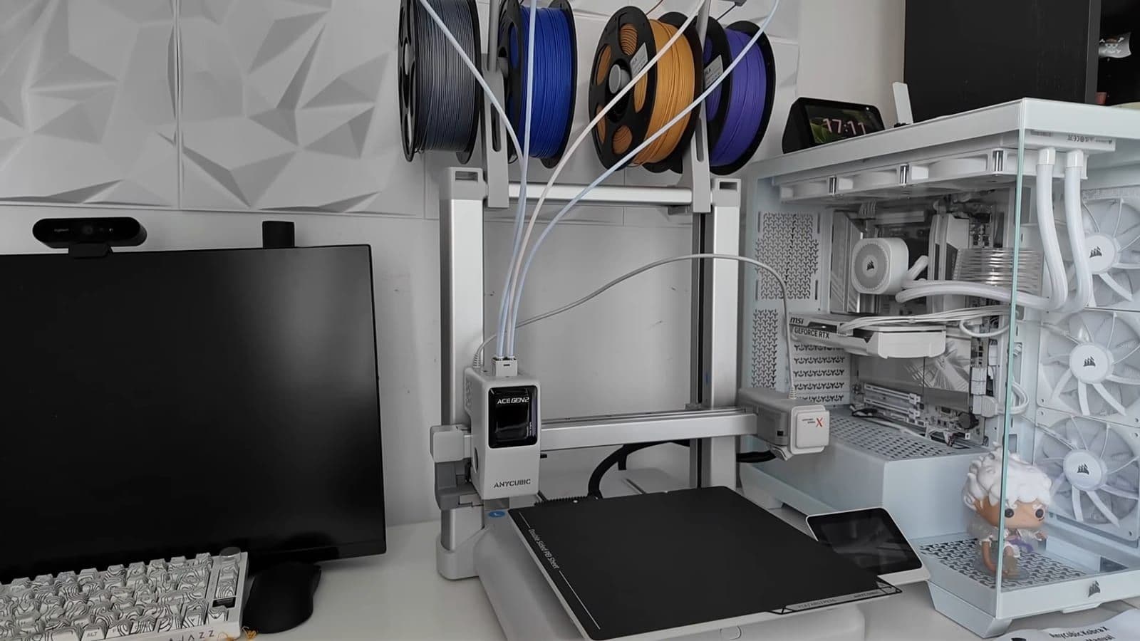 Anycubic Kobra X op een bureau met vier filamentrollen in grijs, blauw, oranje en paars bovenop de printer
