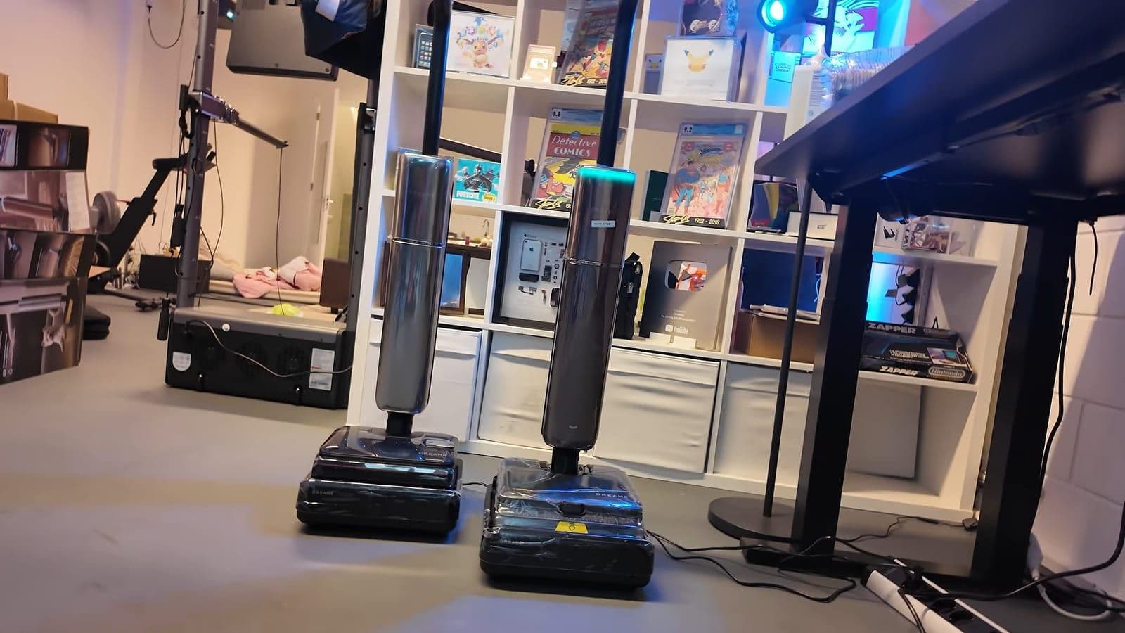 De Dreame T16 Pro Heat en T16 Pro Steam staan naast elkaar in hun stations in een studio, de rechter heeft een oplichtende blauwe ring bovenaan
