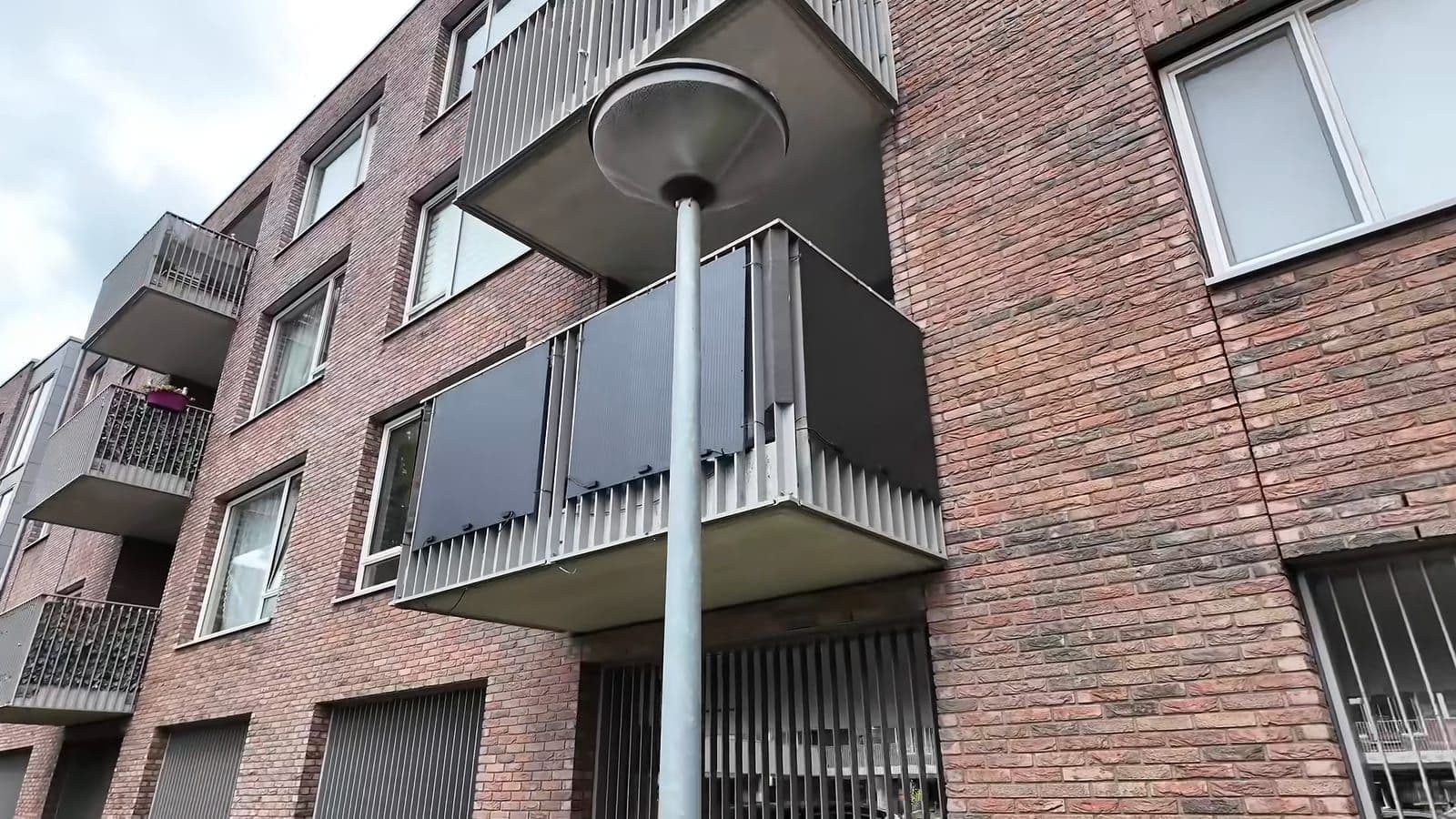 Vier zwarte zonnepanelen gemonteerd aan het balkonhek van een appartementencomplex