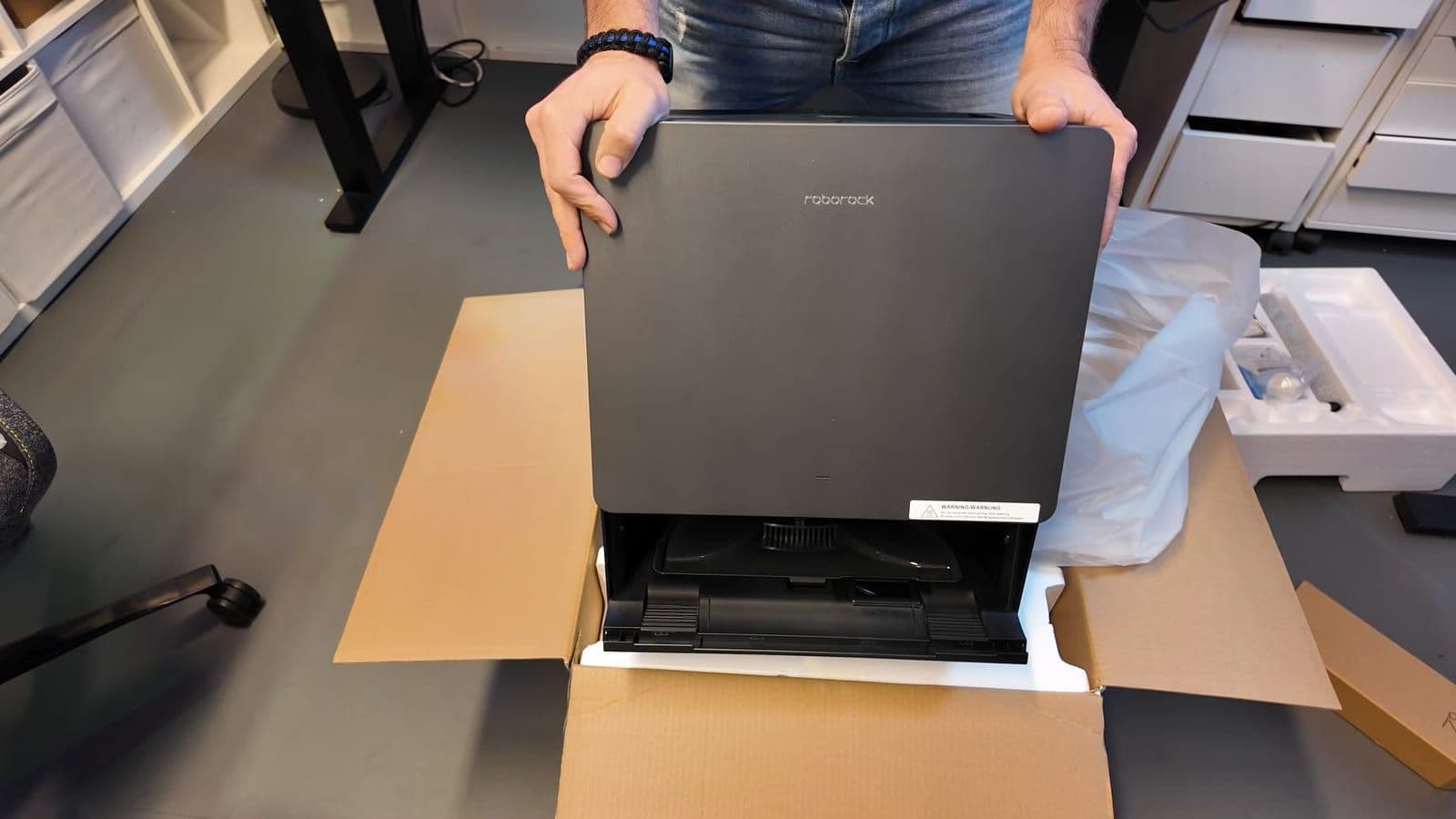 Zwart Roborock-dock wordt uit een kartonnen doos getild