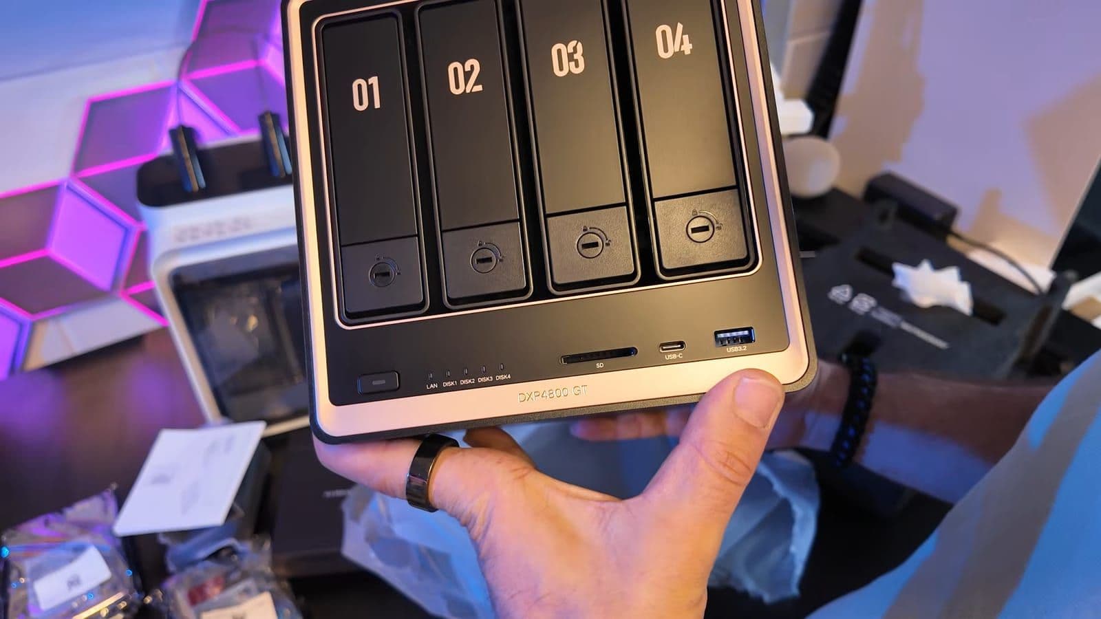 Hand houdt de voorkant van de UGREEN DXP4800 GT vast met vier genummerde drive bays, SD-slot, USB-C en USB-A