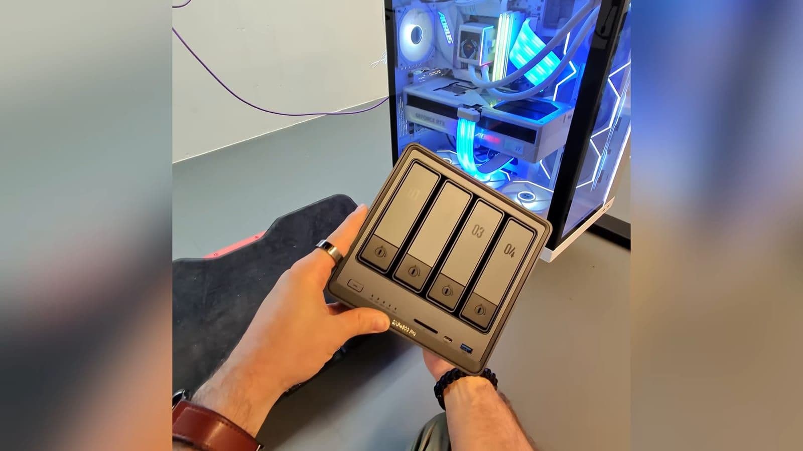 Zino holding the dark grey UGREEN DXP4800 Pro four bay NAS in his hands next to a desktop PC